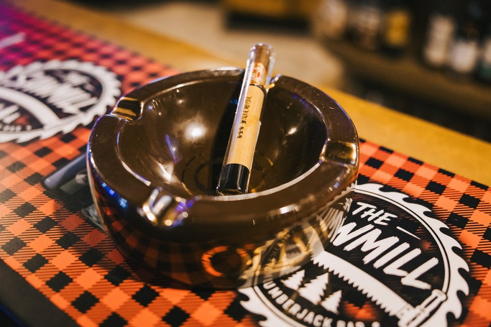 A cigar resting in an ashtray on a buffalo plaid Sawmill bar mat