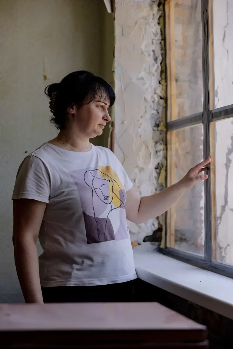 A resident at a kindergarten in Nikopol, Ukraine, standing beside a transparent emergency replacement window installed by Insulate Ukraine.
