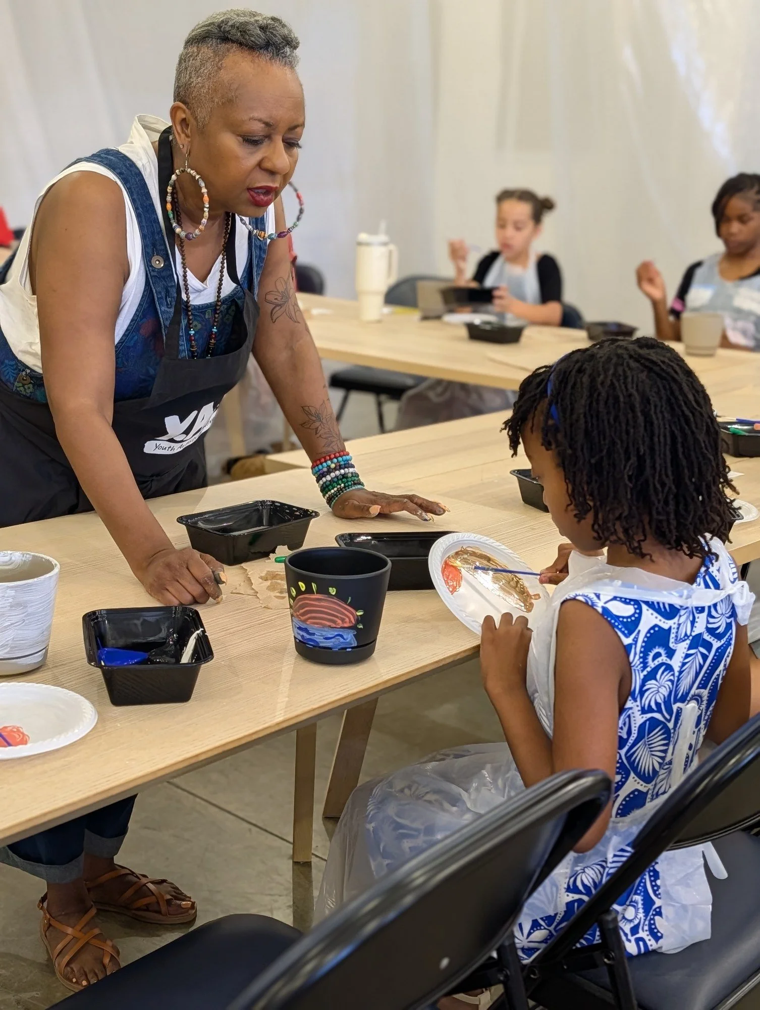A teaching artist guides a young participant through a painting activity.