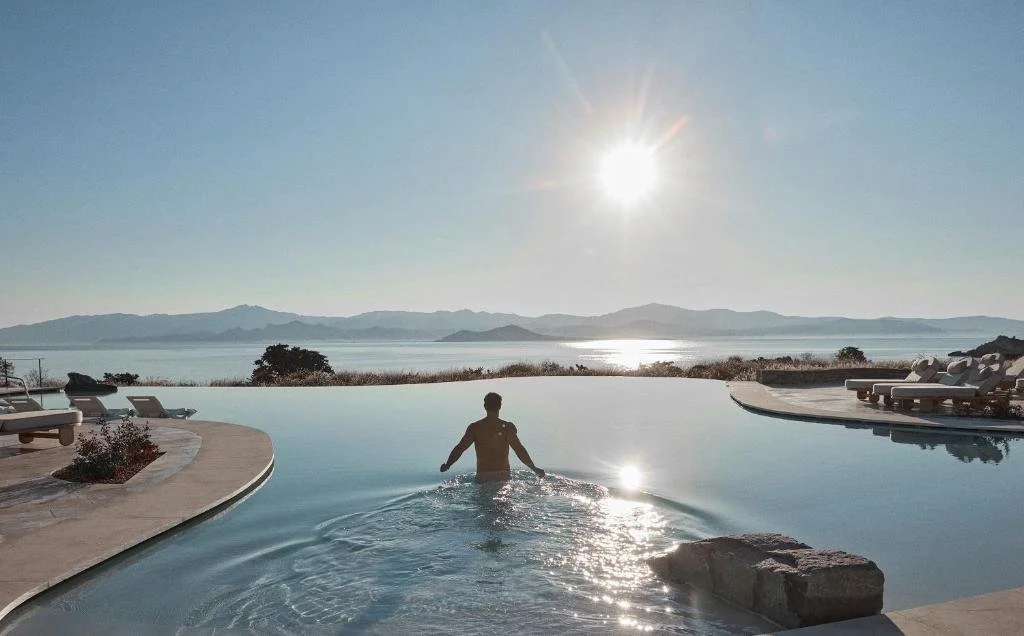Vione Paros infinity pool with panoramic Aegean Sea view and sunburst over distant island mountains