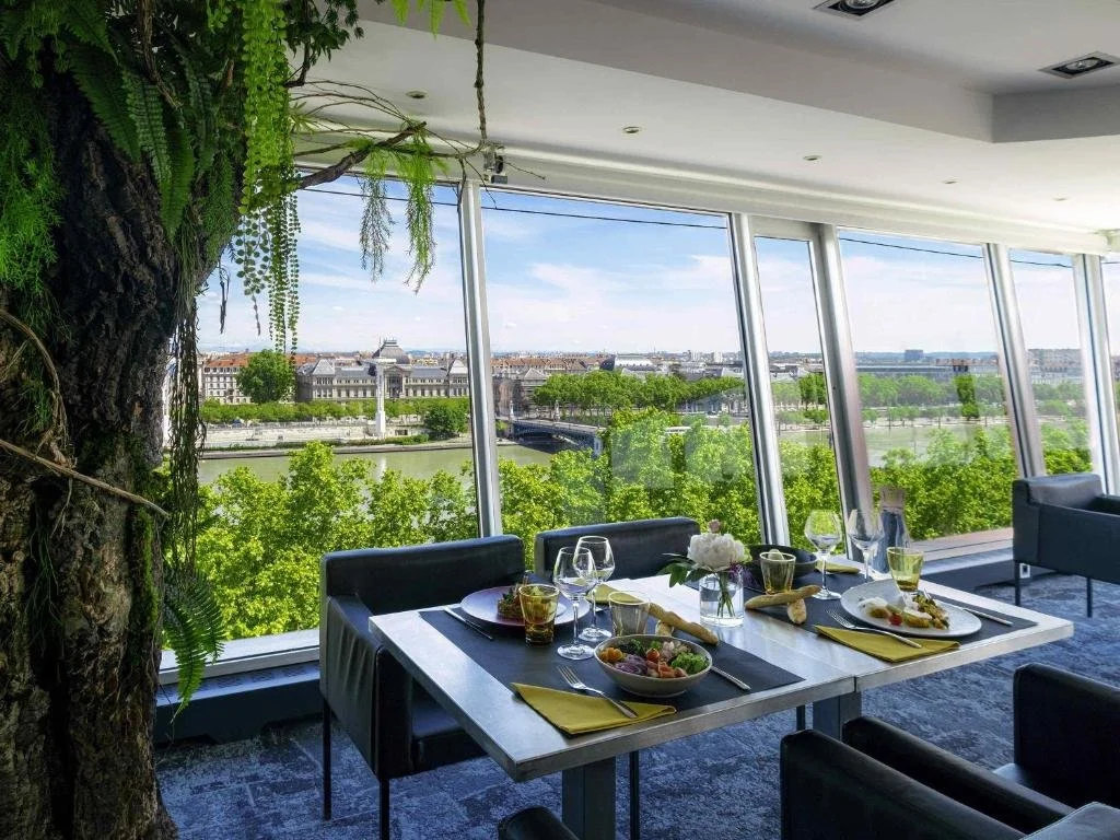 Sofitel Lyon Bellecour Les 3 Dômes restaurant dining table with floor-to-ceiling windows overlooking the Rhône and Lyon city skyline