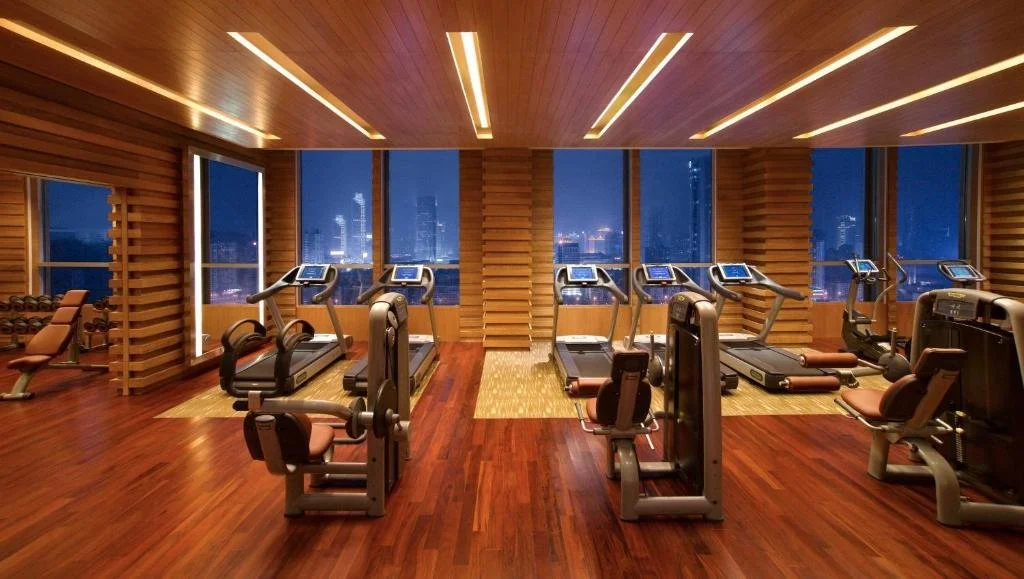 Grand Hyatt Guangzhou high-floor fitness centre at night with wood-panelled walls and a row of treadmills facing full-height windows and the lit Guangzhou skyline