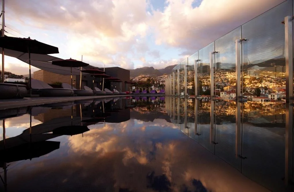 The Vine Hotel Funchal rooftop infinity pool at dusk reflecting the city skyline and Funchal mountains