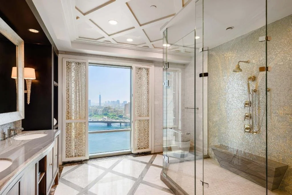 The St. Regis Cairo luxury suite bathroom with gold fixtures and panoramic view of the Nile River, Qasr El Nil Bridge and Cairo Tower