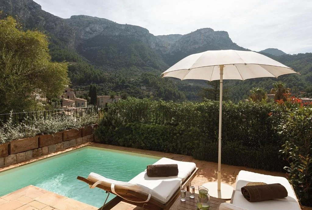 La Residencia A Belmond Hotel Deià private pool terrace with sun loungers and Tramuntana mountain ridge and village rooftops behind