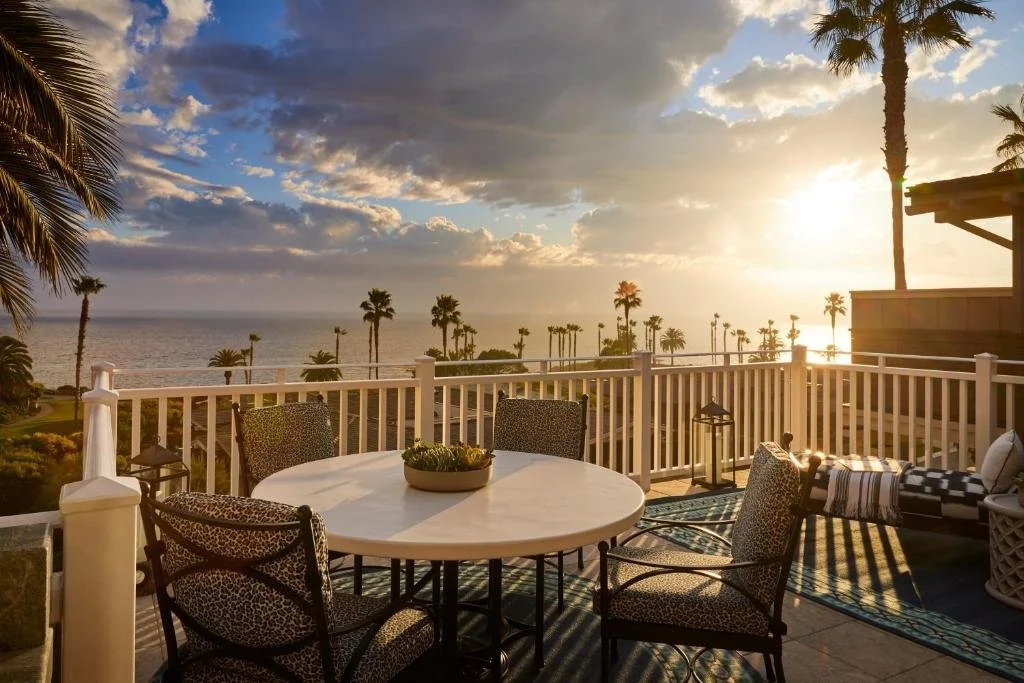 Montage Laguna Beach private terrace with outdoor dining table and Pacific Ocean sunset view framed by palm trees