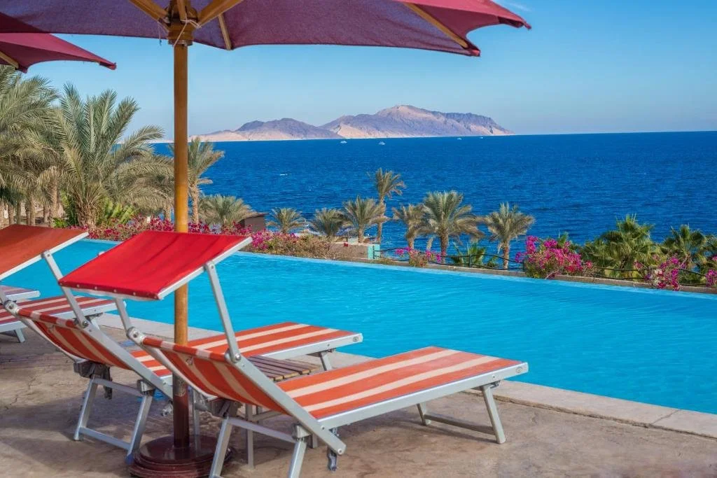 Grand Rotana Resort Sharm El Sheikh pool deck with striped sunloungers facing the Red Sea and Tiran Island on the horizon