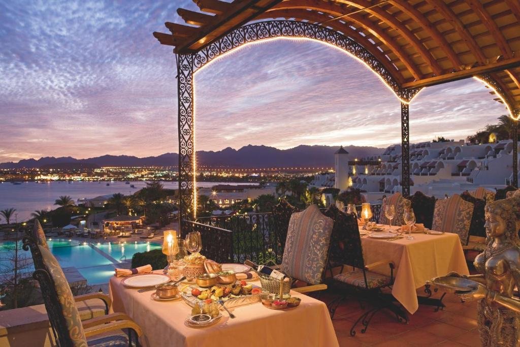 Mövenpick Resort Sharm El Sheikh open-air restaurant terrace at dusk with Naama Bay and Sinai mountains in the background