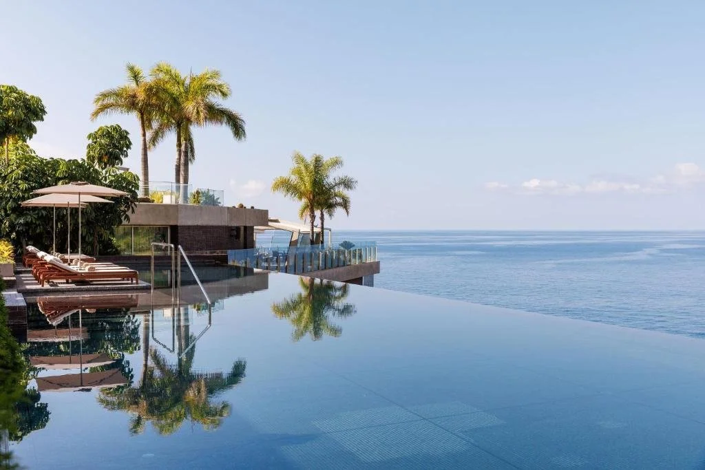 Saccharum Madeira infinity pool with palm tree reflections and Atlantic Ocean horizon, Calheta