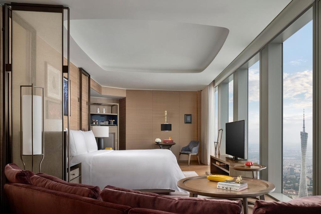 Rosewood Guangzhou guest room with warm neutral tones and a full-height window wall, the Canton Tower rising from the cityscape far below in clear daylight