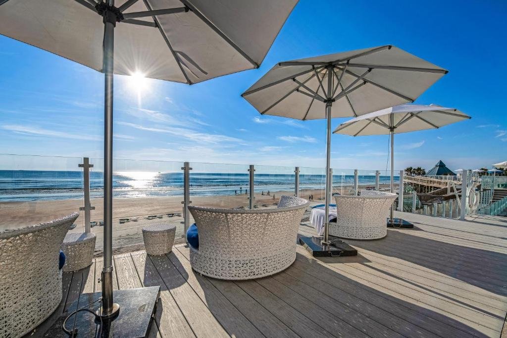 Daytona Grande Oceanfront Resort Daytona Beach beachfront deck with white wicker lounge chairs and large umbrellas overlooking the sand and ocean