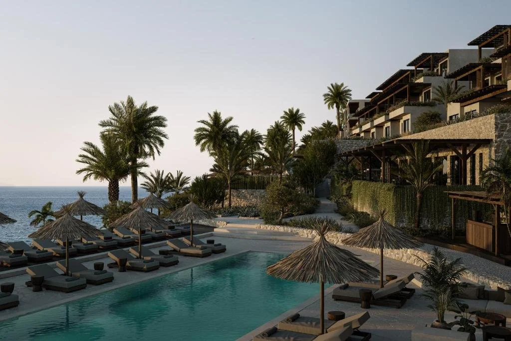 OKU Bodrum poolside area with thatched parasols, palm trees, and terraced hotel building overlooking the Aegean Sea at dawn