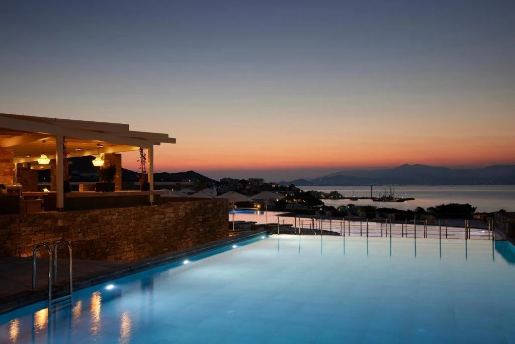 Summer Senses Luxury Resort Paros infinity pool at sunset with bay town lights sailboats and orange sky