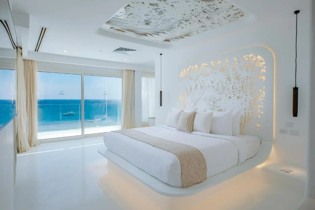 Meraki Resort Sharm El Sheikh white suite with sculptural gold coral headboard and floor-to-ceiling windows overlooking the Red Sea