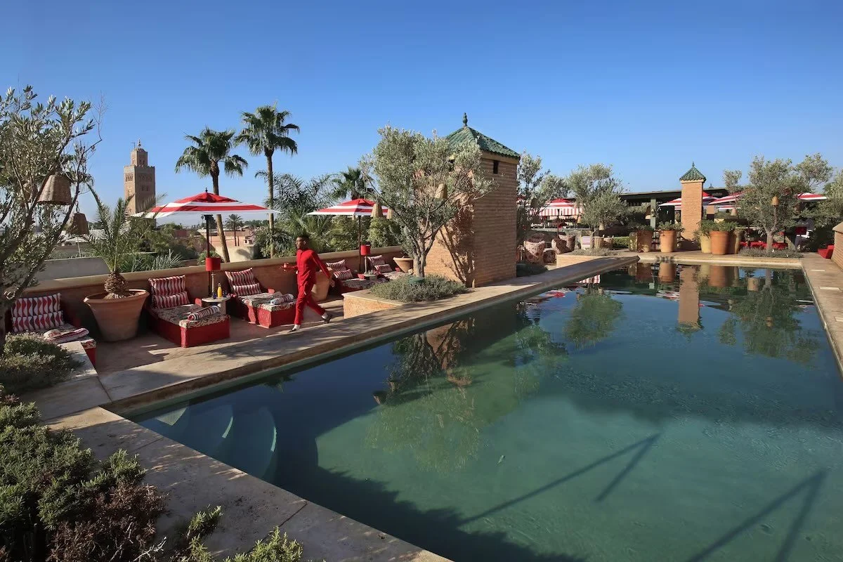 El Fenn Marrakech rooftop pool with Moroccan pavilion towers and the Koutoubia Mosque minaret visible through the palms