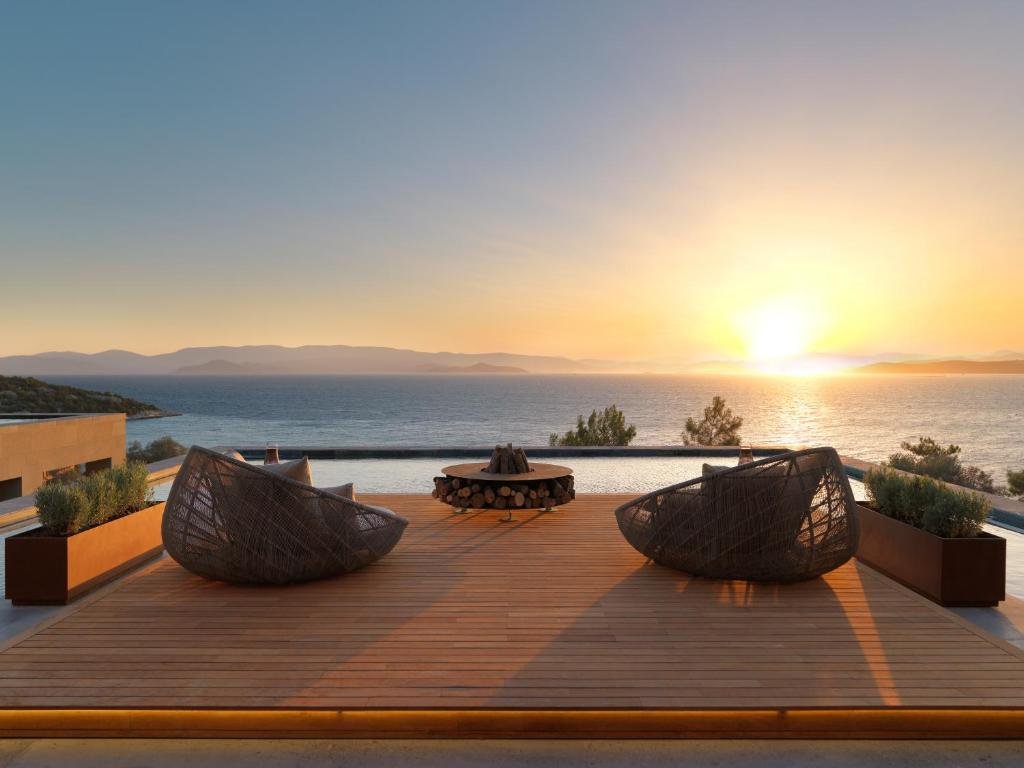 Mandarin Oriental Bodrum wooden deck terrace with rattan lounge chairs and fire pit overlooking infinity pool and Aegean Sea at sunset