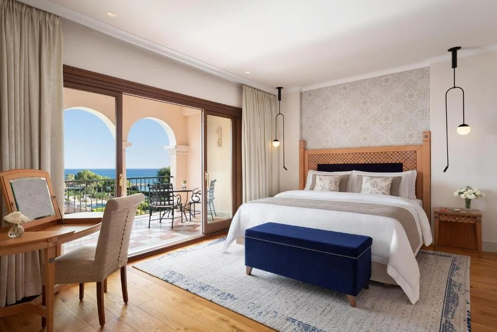 The St. Regis Mardavall Mallorca Resort bedroom with arched terrace doors open to balcony table and Mediterranean sea view
