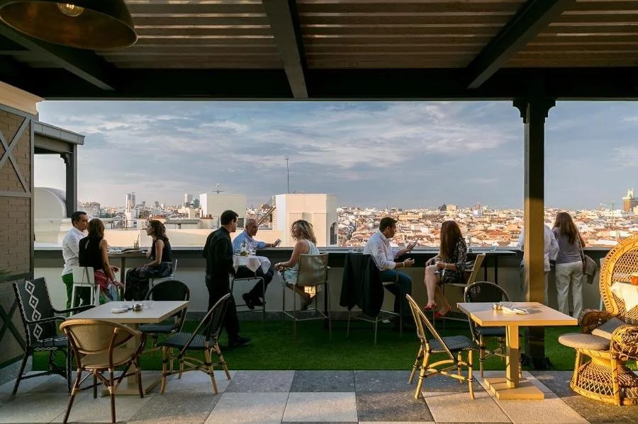 Hotel Emperador Madrid covered rooftop terrace at dusk with guests and Cuatro Torres business district skyline view