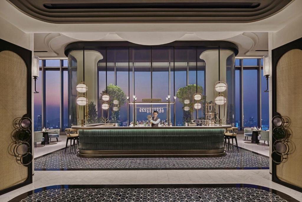 Shangri-La Nanshan Shenzhen hotel bar at dusk, curved green counter with brass globe pendants and floor-to-ceiling windows over the city at sunset