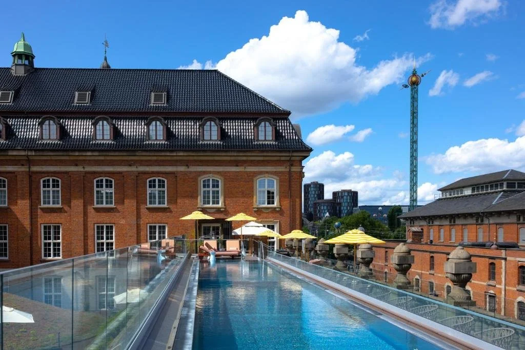 Villa Copenhagen rooftop pool with 1912 neo-baroque building facade, yellow umbrellas, and Tivoli Gardens StarFlyer tower