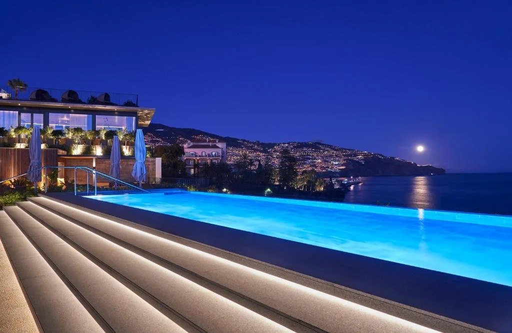 Les Suites at The Cliff Bay Funchal infinity pool illuminated at night with Funchal city lights and moonlit Atlantic Ocean