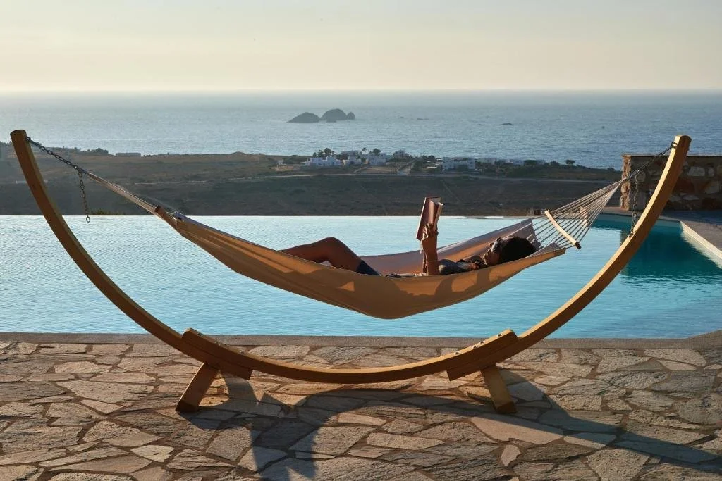 Mythic Paros arched hammock by infinity pool with wide Aegean Sea view and rocky islets at golden hour
