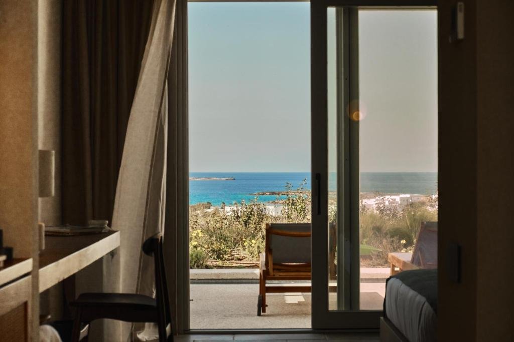 Ovea Paros Paros hotel room with sliding glass doors opening to terrace and Aegean Sea view with beach and islet