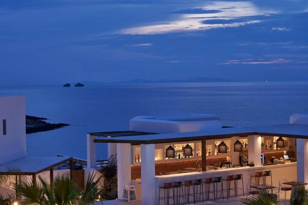 Andronis Minois Paros outdoor bar at dusk with pendant lights and Aegean Sea view with rocky islets in distance