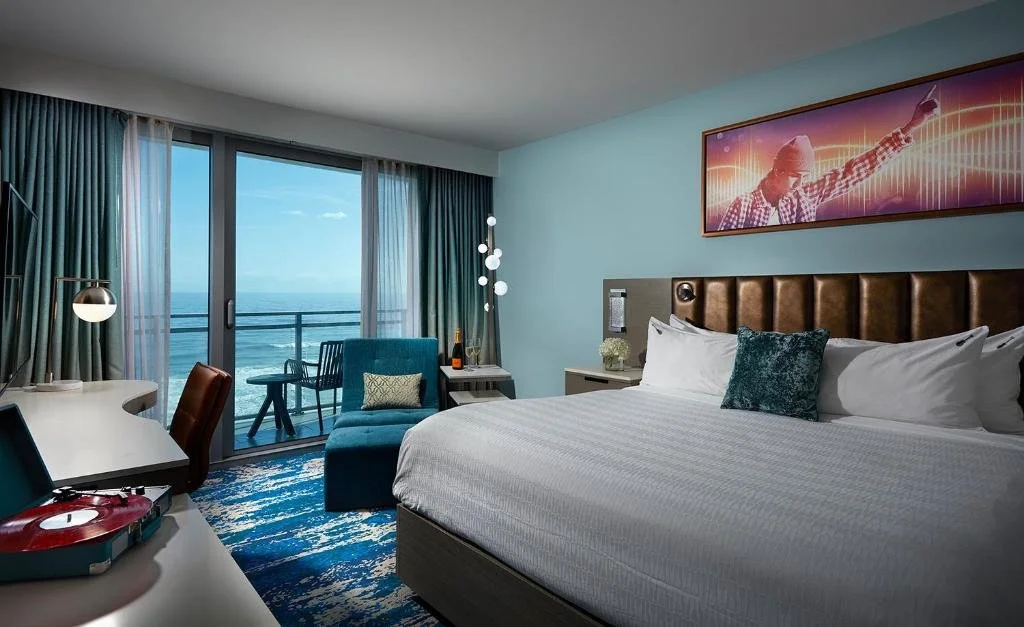 Hard Rock Hotel Daytona Beach king room with vinyl record player, rock art above headboard, and open balcony with direct Atlantic Ocean view