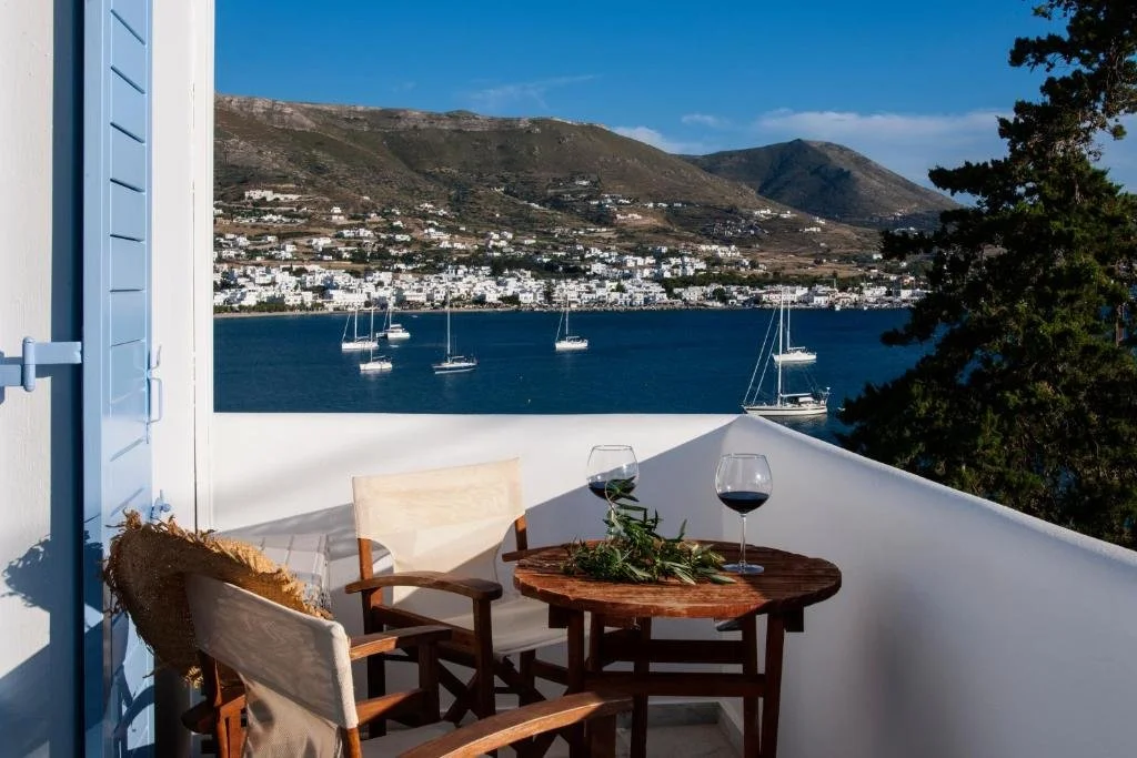 Parian Village Beach Hotel Paros balcony with wine glasses overlooking Parikia bay with sailing boats and hillside