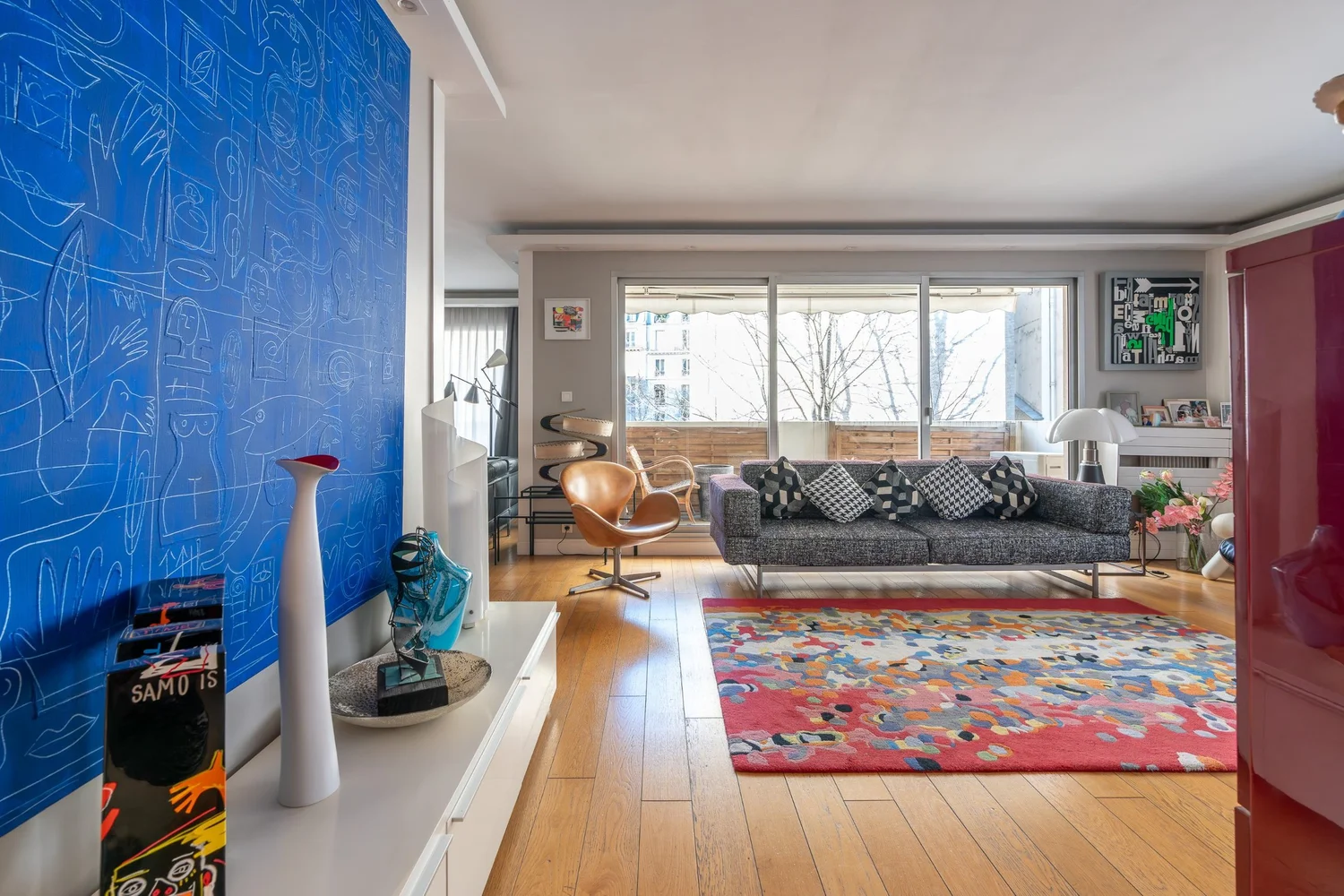 Séjour lumineux avec parquet en chêne, baie vitrée sur terrasse, fauteuil en cuir et œuvres d’art