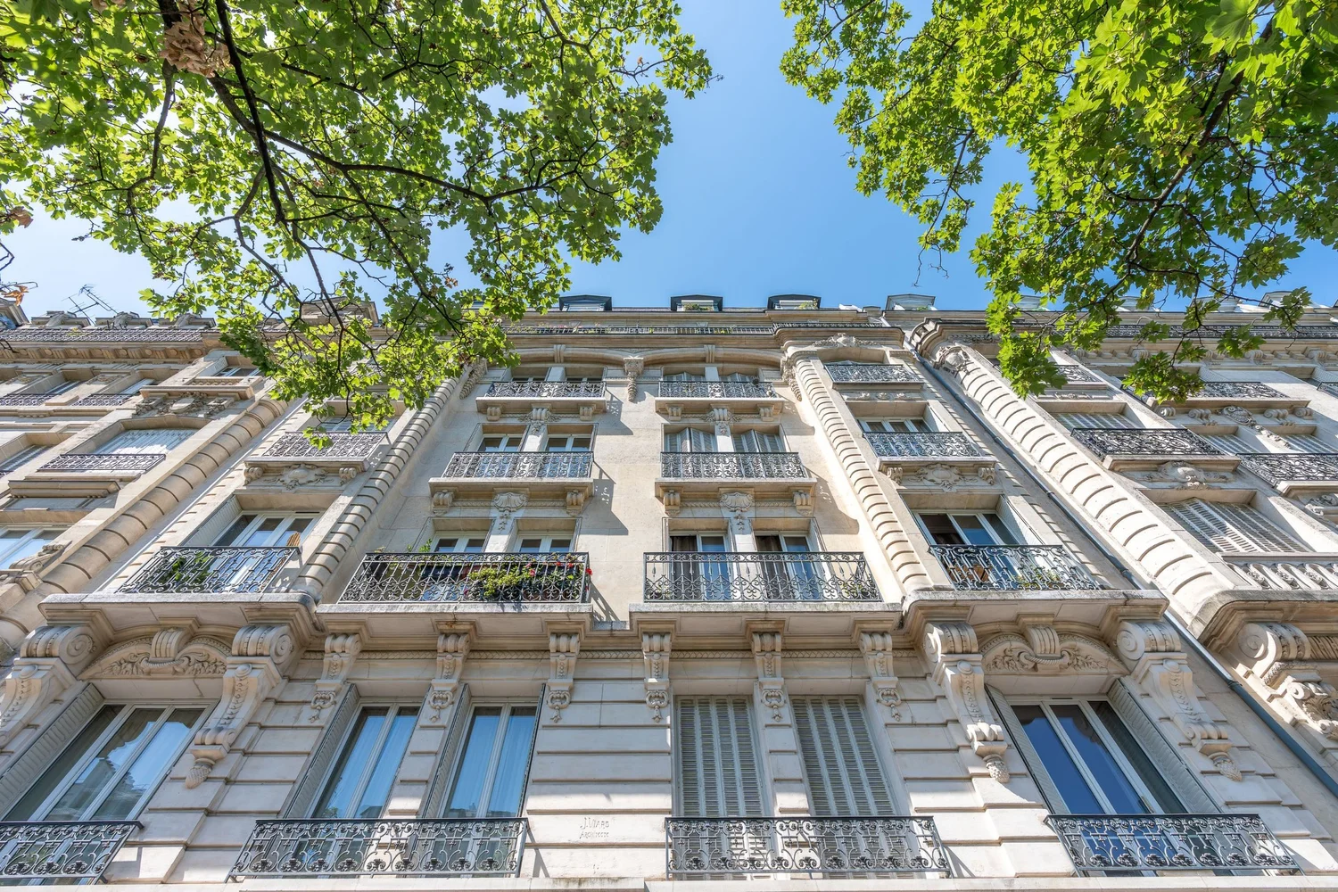 Façade haussmannienne en pierre de taille vue d’en bas, balcons en fer forgé et platanes