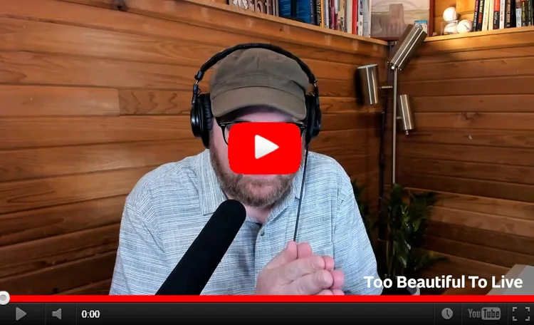 YouTube still image of Andrew holding his hands together in a prayer-like gesture  in his studio