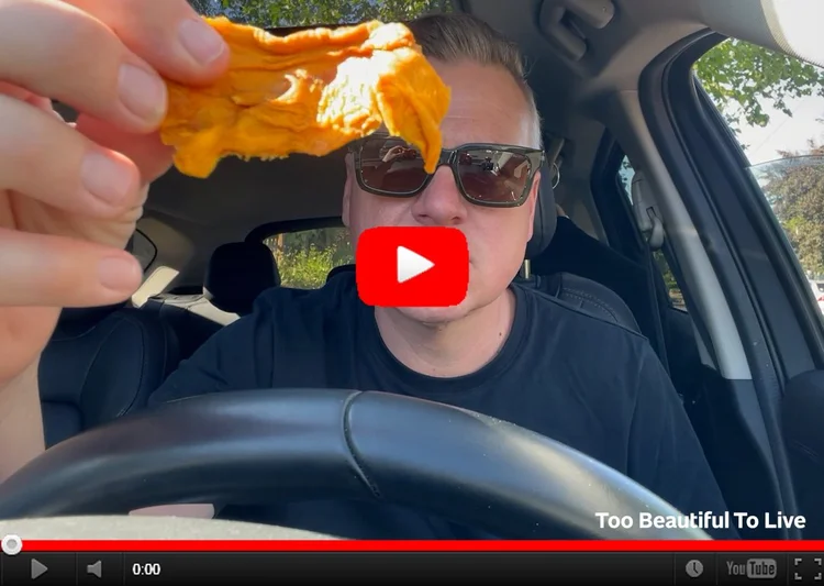 YouTube still image of Luke in his car holding a piece of dried fruit up to the camera. 