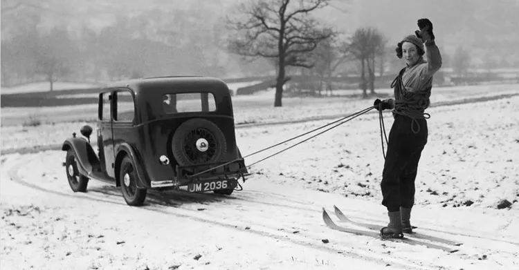 Vintage black and white photo of a person on skis getting pulled by a 1940s car