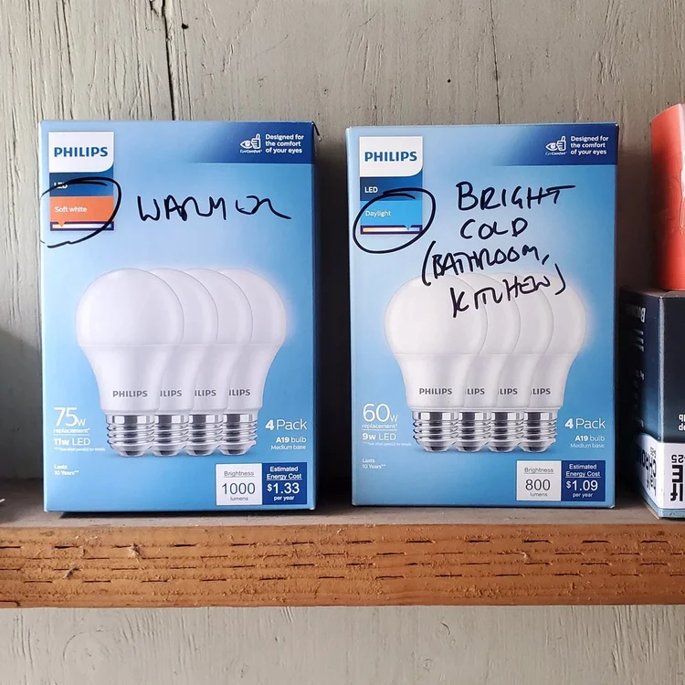 Photo of two boxes of light bulbs with handwritten scrawls that say "Warmer" on one and "Bright cold (kitchen bathroom)" on the other.