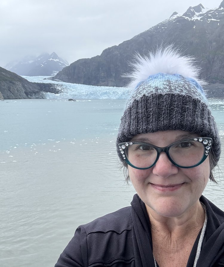 Photo of listener Amanda standing outsie in the winter in front of a ocean and mountains. 