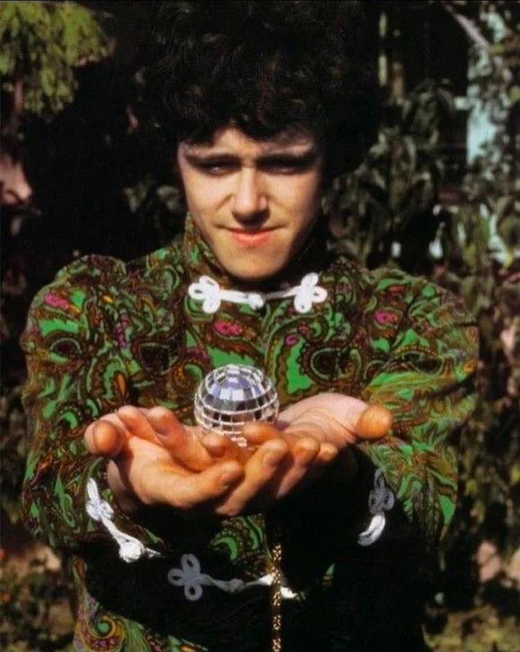 photo of the musician donovan holding a tiny little disco ball in his outstretched hands. 