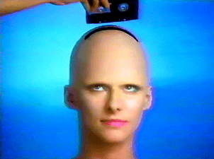 1980s animated gif of someone sliding a sony cassette tape into the top of a bald, animatronic head