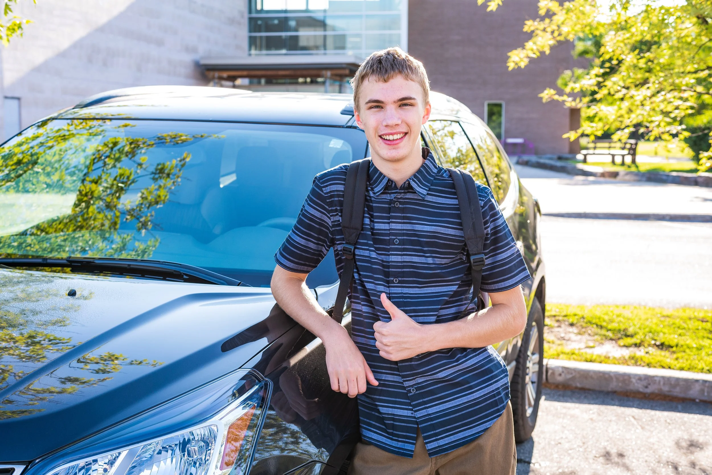 Smiling teen driver standing next to his car outside school