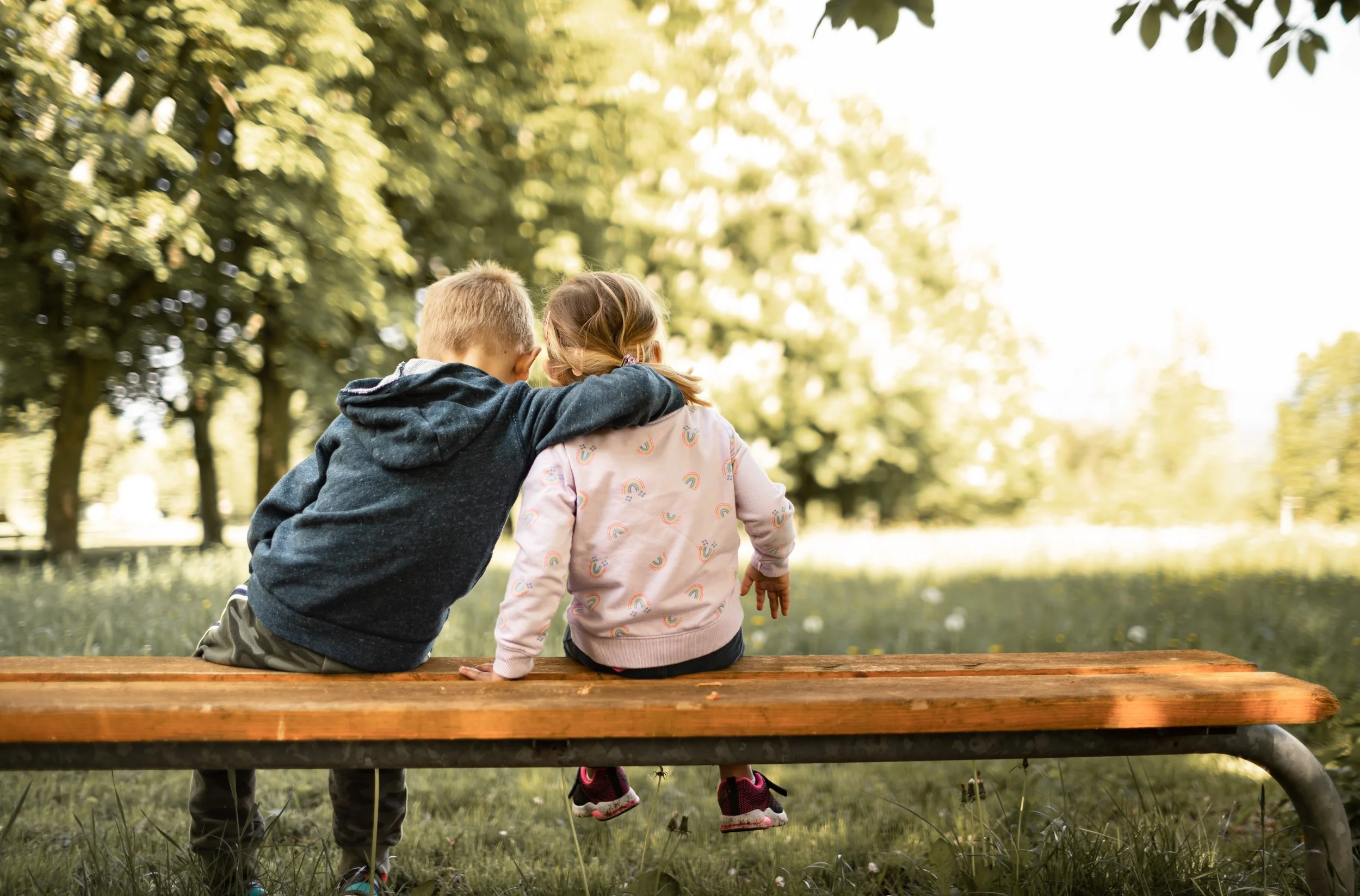 Two young siblings sitting together on a bench outdoors