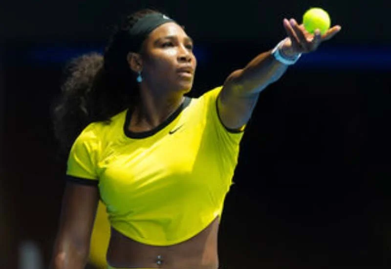 Serena Williams with a tennis ball in her outstretched hand.