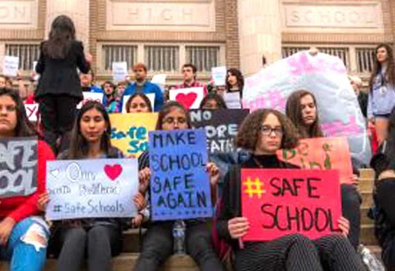 A group of school-aged children sitting on steps of a Tucson Magnet School holding signs demanding school safety measures.