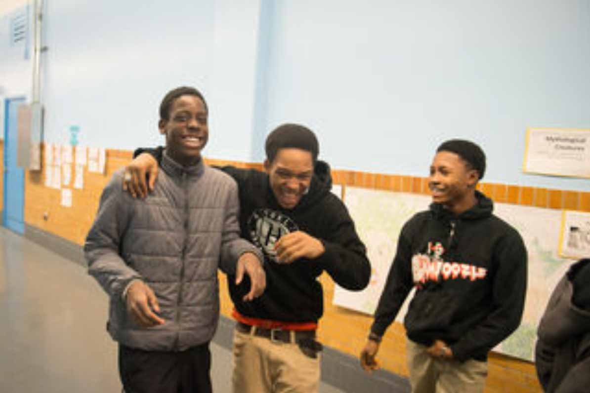 Three adolescent boys, two with their arms around each other, laugh out loud as they walk down the hallway at Chancellor Avenue School in Newark, New Jersey.