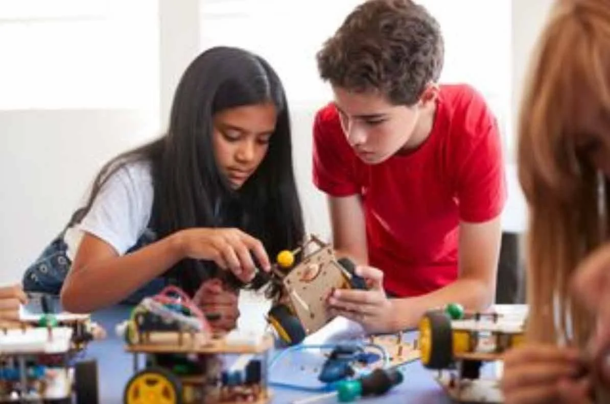 Two adolescents, a girl and a boy, build a small robot together.