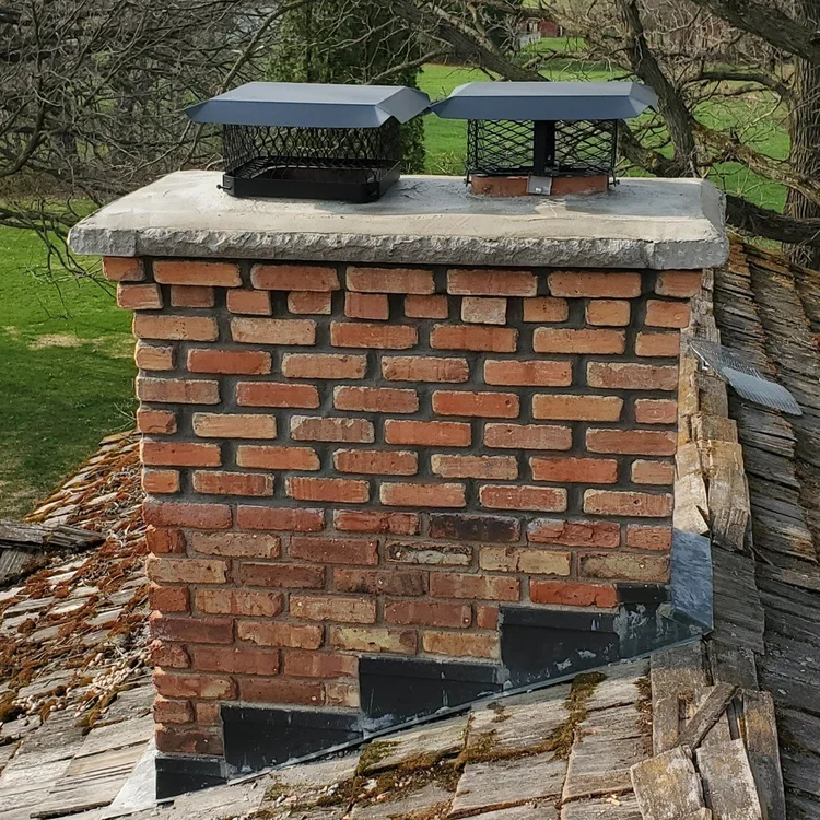 A brick chimney with a crown we rebuilt, with an overhang, two black caps and new flashing