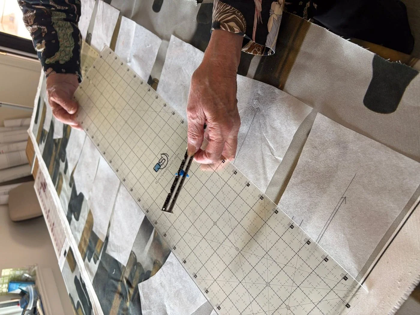 Hands marking a paper pattern on a gridded cutting mat.