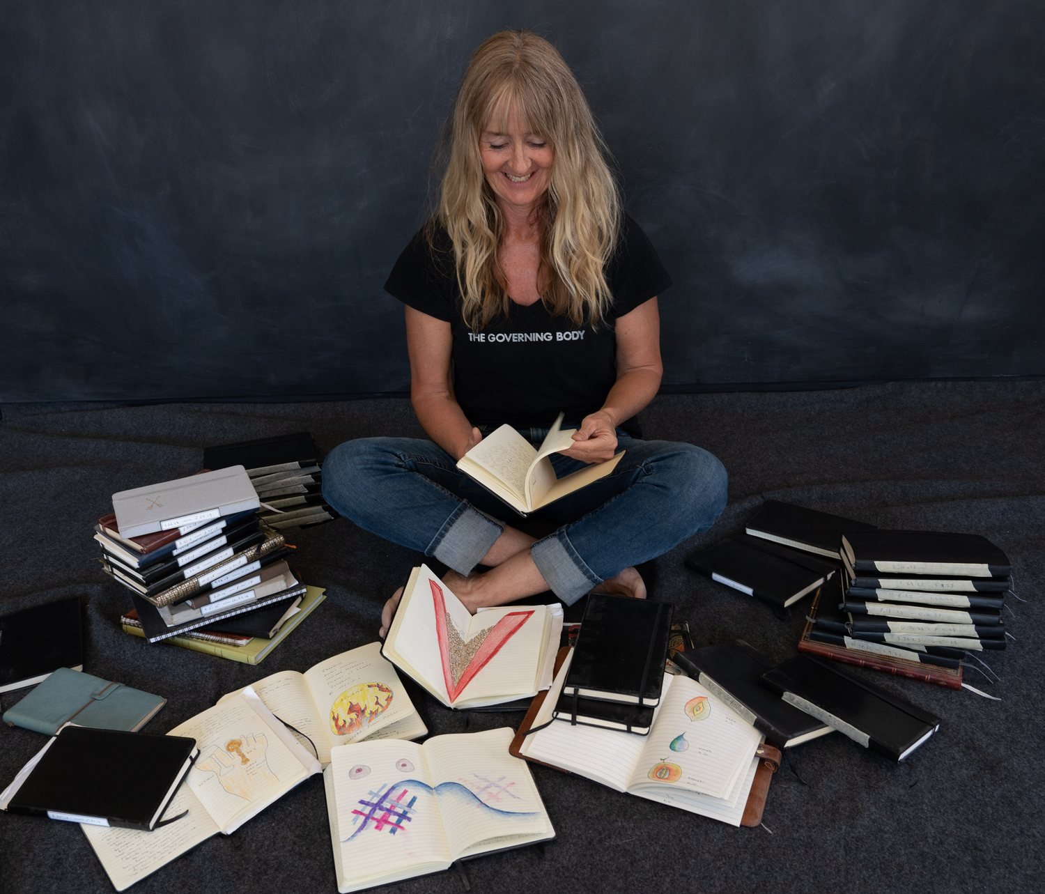 Christie Green seated on the floor, reading, surrounded by her dream journals.