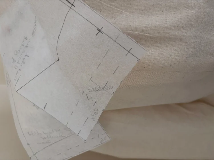 A marked paper pattern pinned to pale cloth.