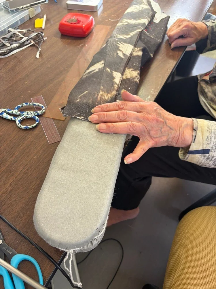 Hands working a seam over a sleeve board.